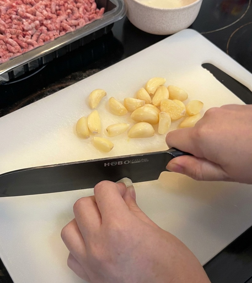 Eine Nahaufnahme von einem großen Haufen frischer Knoblauchzehen, die auf einem sauberen weißen Schneidebrett grob gehackt werden.