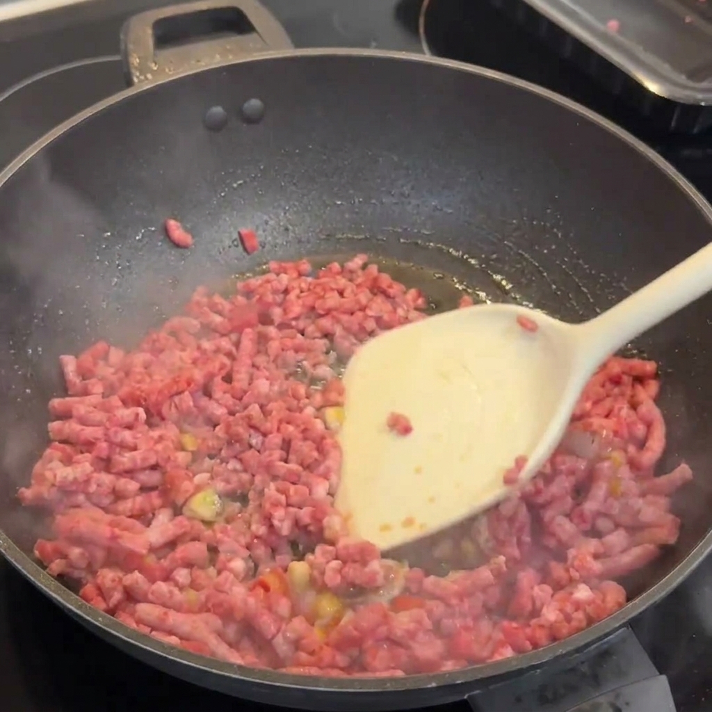 Wagyu-Rinderhackfleisch bräunt im Wok mit Knoblauch und Chilis und wird mit einem weißen Pfannenwender zerkleinert.