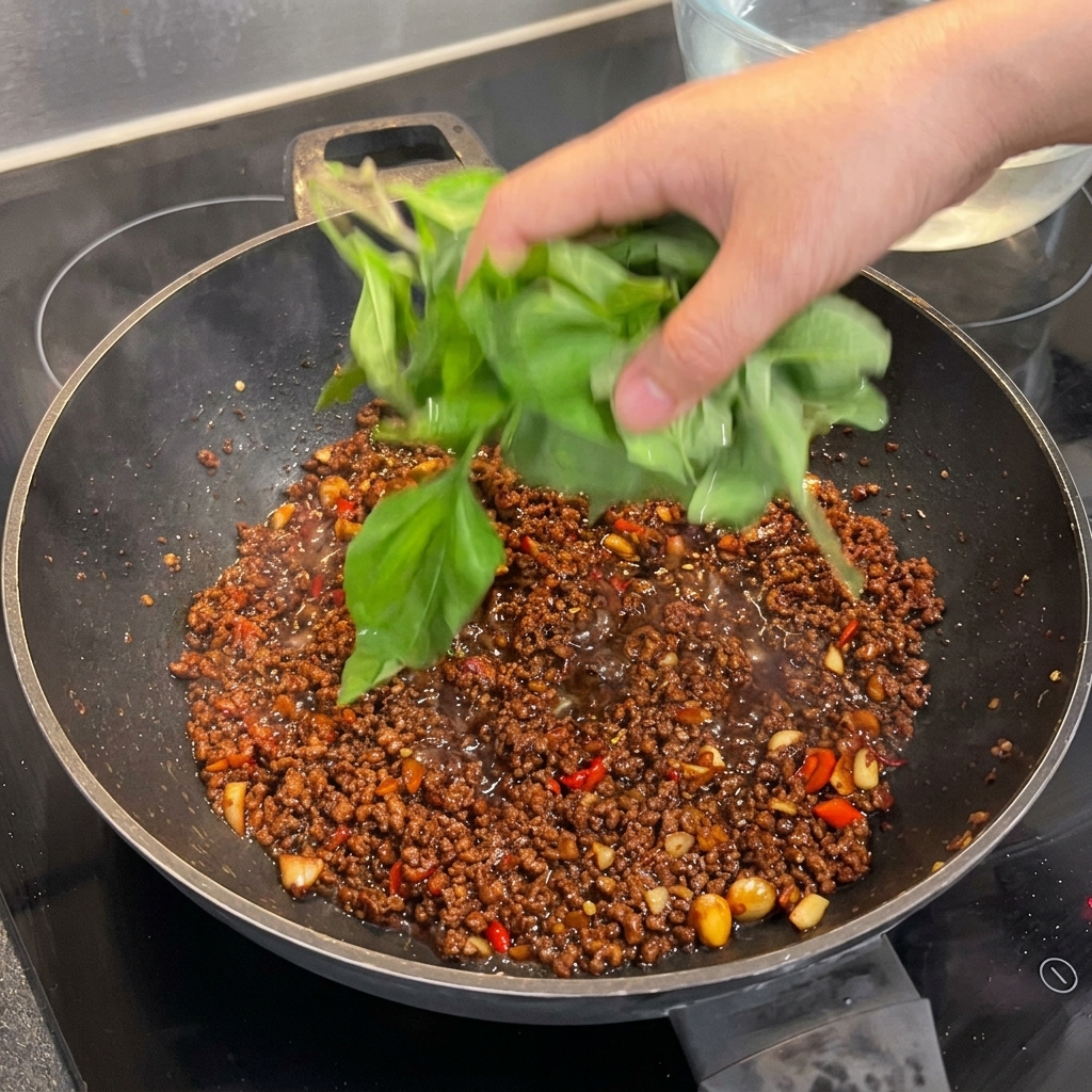 Eine große Handvoll frischer Blätter vom heiligen Basilikum wird in den Wok zum gewürzten Fleisch gegeben, bereit zum Welken.