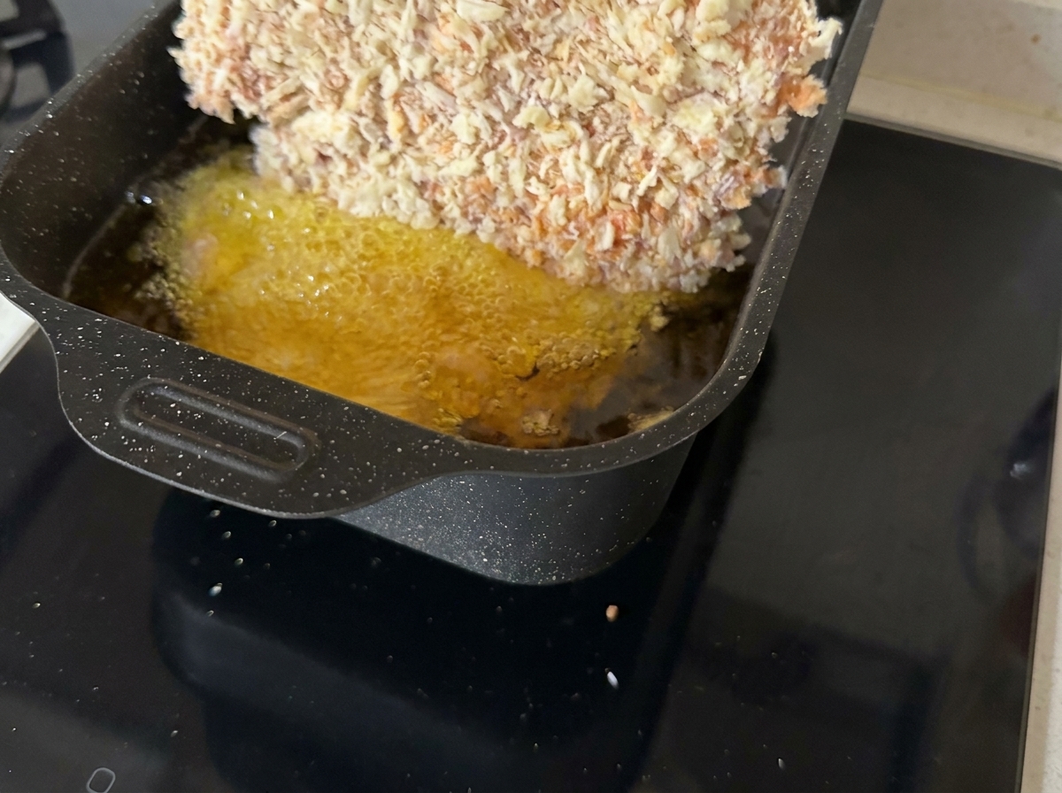 Ein paniertes Schnitzel brät in einer flachen Pfanne in heißem Öl.