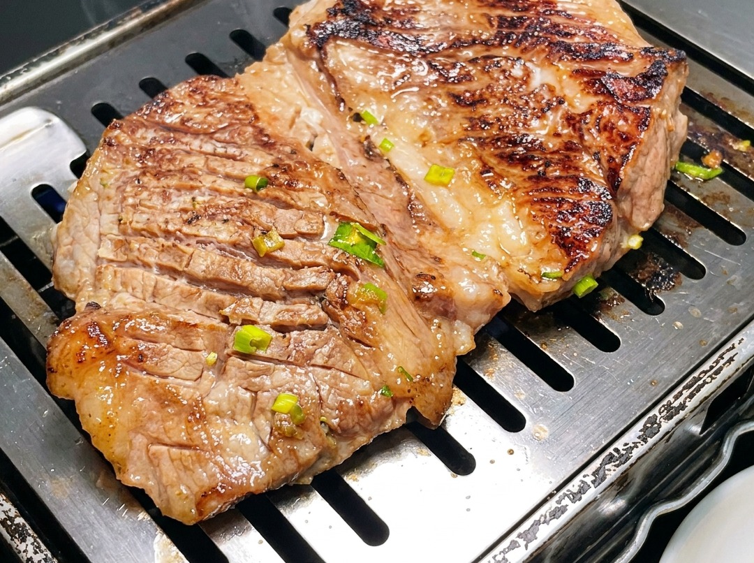 Nahaufnahme von koreanischen Rinderrippchen, die mit einer Küchenschere direkt in der Grillpfanne in Stücke geschnitten werden.