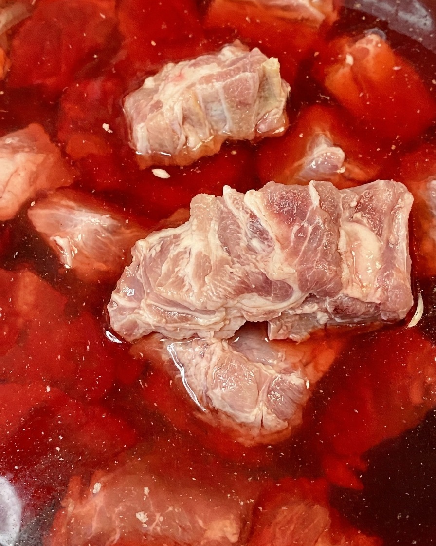 Rohe Schweinewirbelknochen in einer Schüssel mit rötlichem, blutigem Wasser.