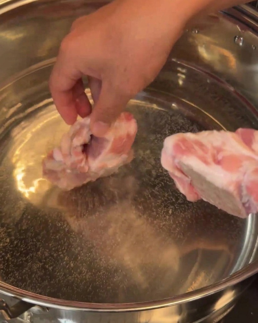 Rohe Schweineknochen werden vorsichtig in einen großen Topf mit Wasser gegeben.