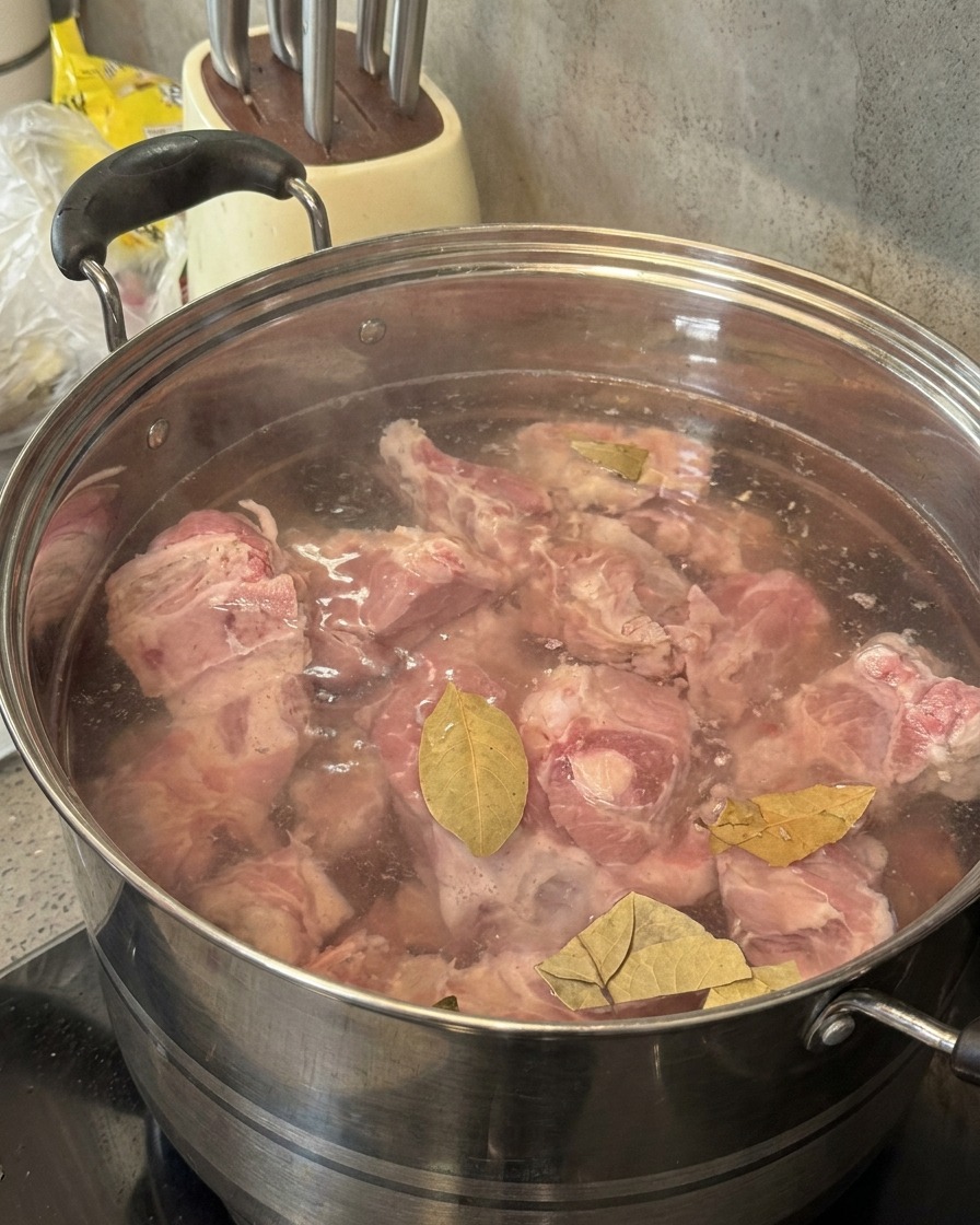 Soju wird aus einer grünen Flasche in einen Topf mit Schweineknochen und Lorbeerblättern gegossen.