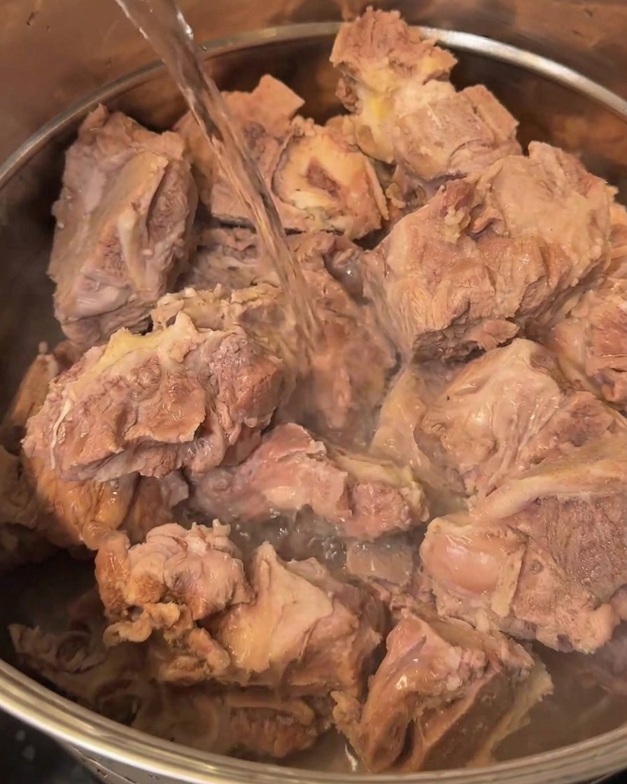 Frisches Wasser wird in einen großen Metalltopf mit den abgespülten Schweineknochen gegossen.