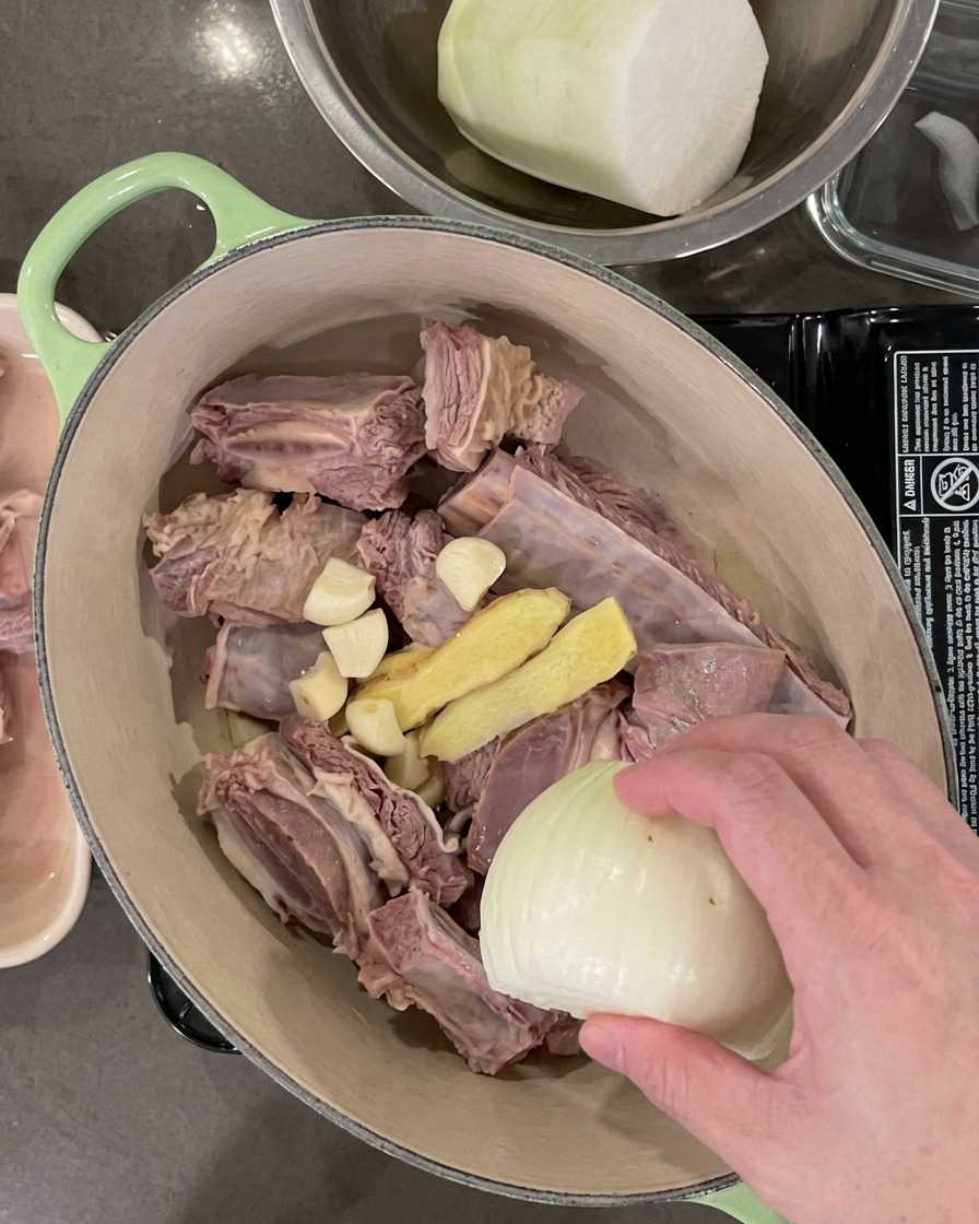Der Topf mit den Rippchen enthält nun auch Knoblauchzehen, Ingwerscheiben, eine Zwiebelhälfte und Frühlingszwiebeln.