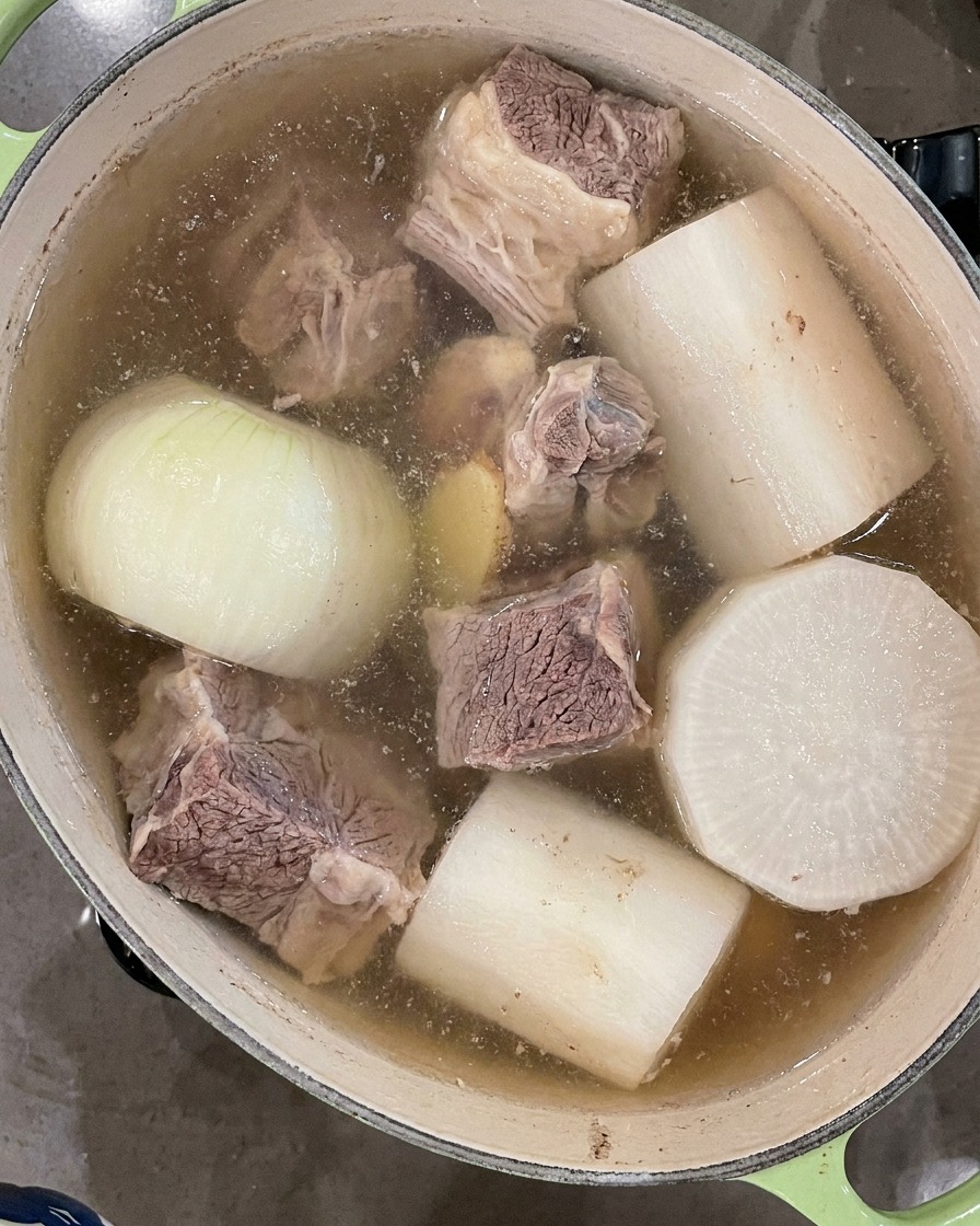 Eine schwarze Schöpfkelle schöpft schwimmenden Schaum von der Oberfläche der kochenden Suppenbrühe.