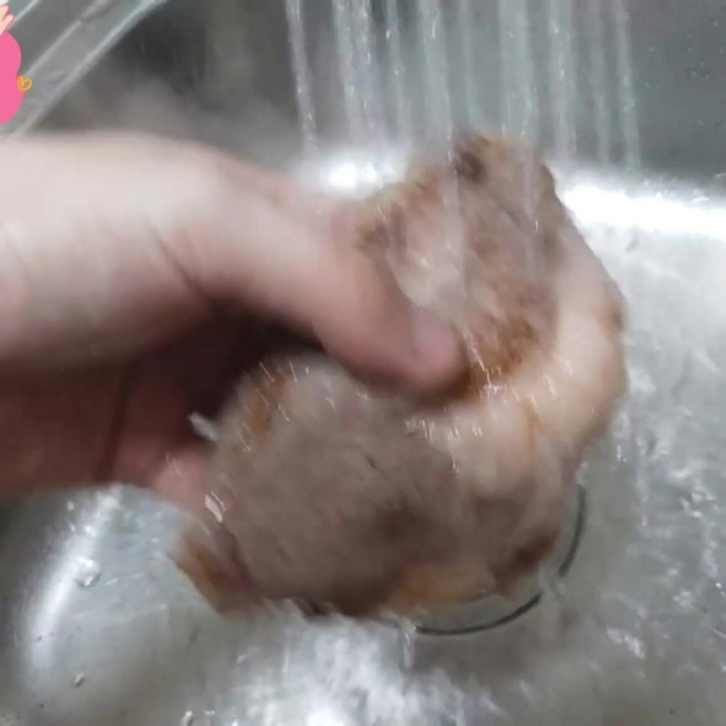 Ein Stück blanchierte Rinderrippe wird im Waschbecken unter fließendes Wasser gehalten.