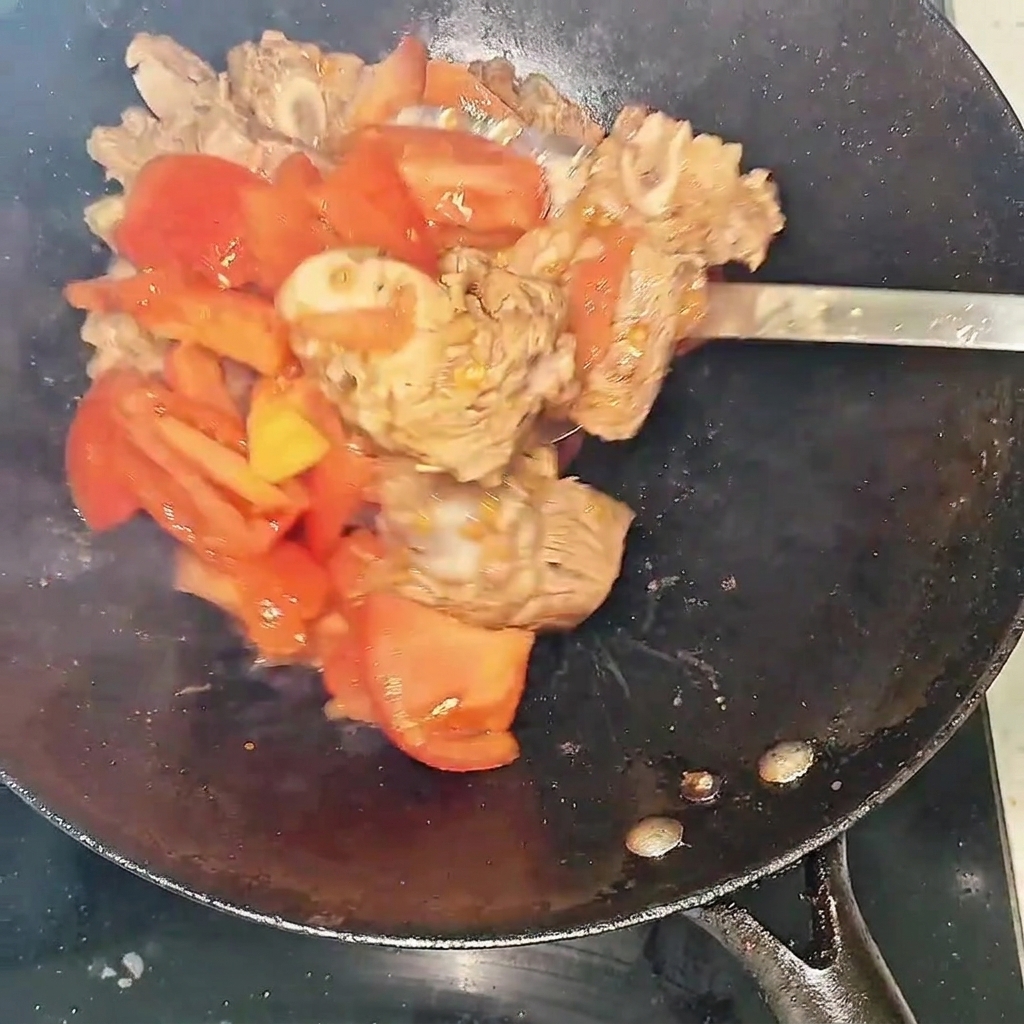 Nahaufnahme von Rinderrippchen und Tomaten im Wok, bei denen sich langsam Flüssigkeit bildet.