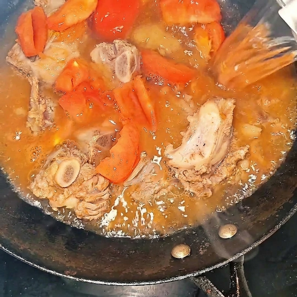 Kochendes Wasser wird in den Wok zu den Rinderrippchen und Tomaten gegossen.