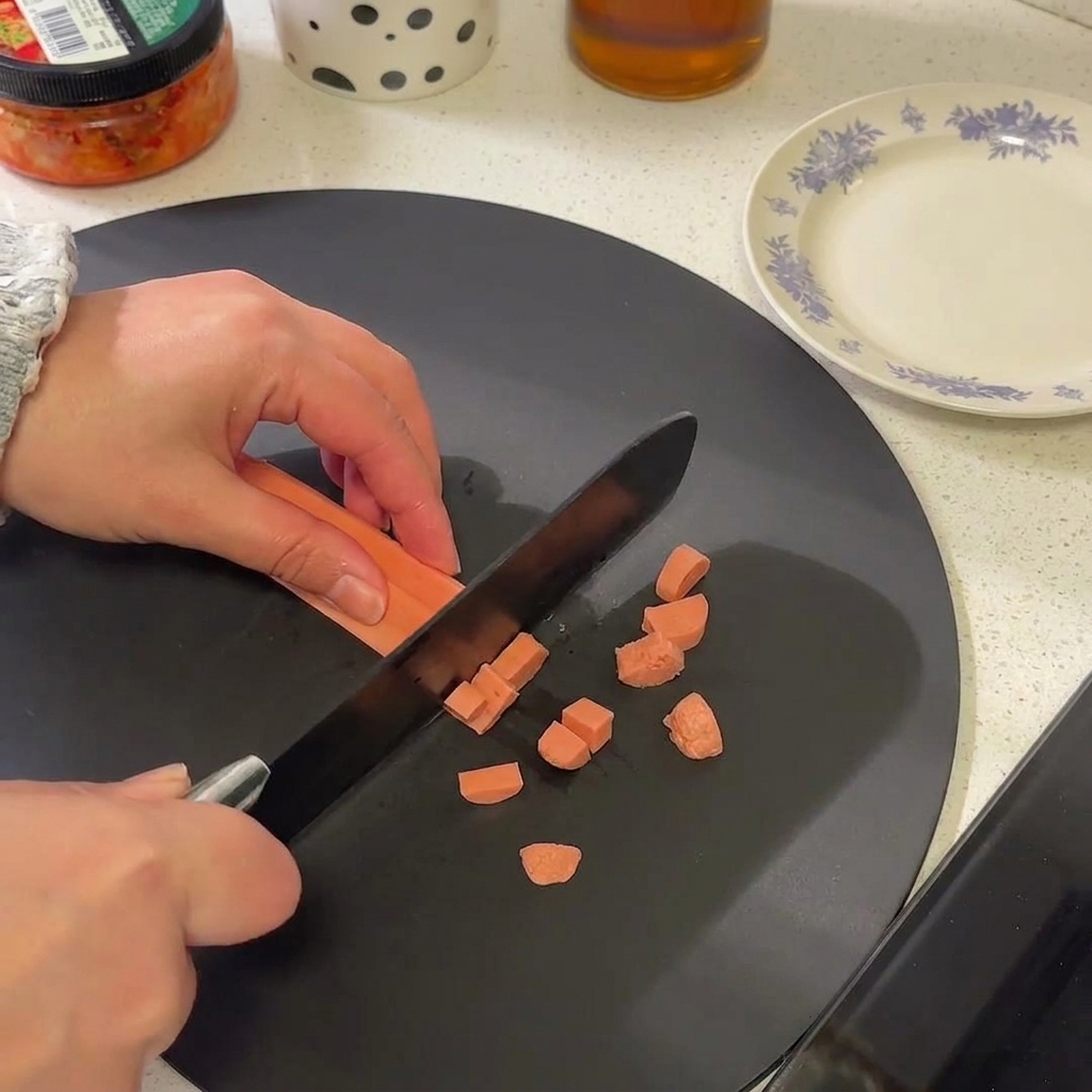 Nahaufnahme einer Wurst, die in kleine Scheiben auf einem schwarzen Schneidebrett geschnitten wird.