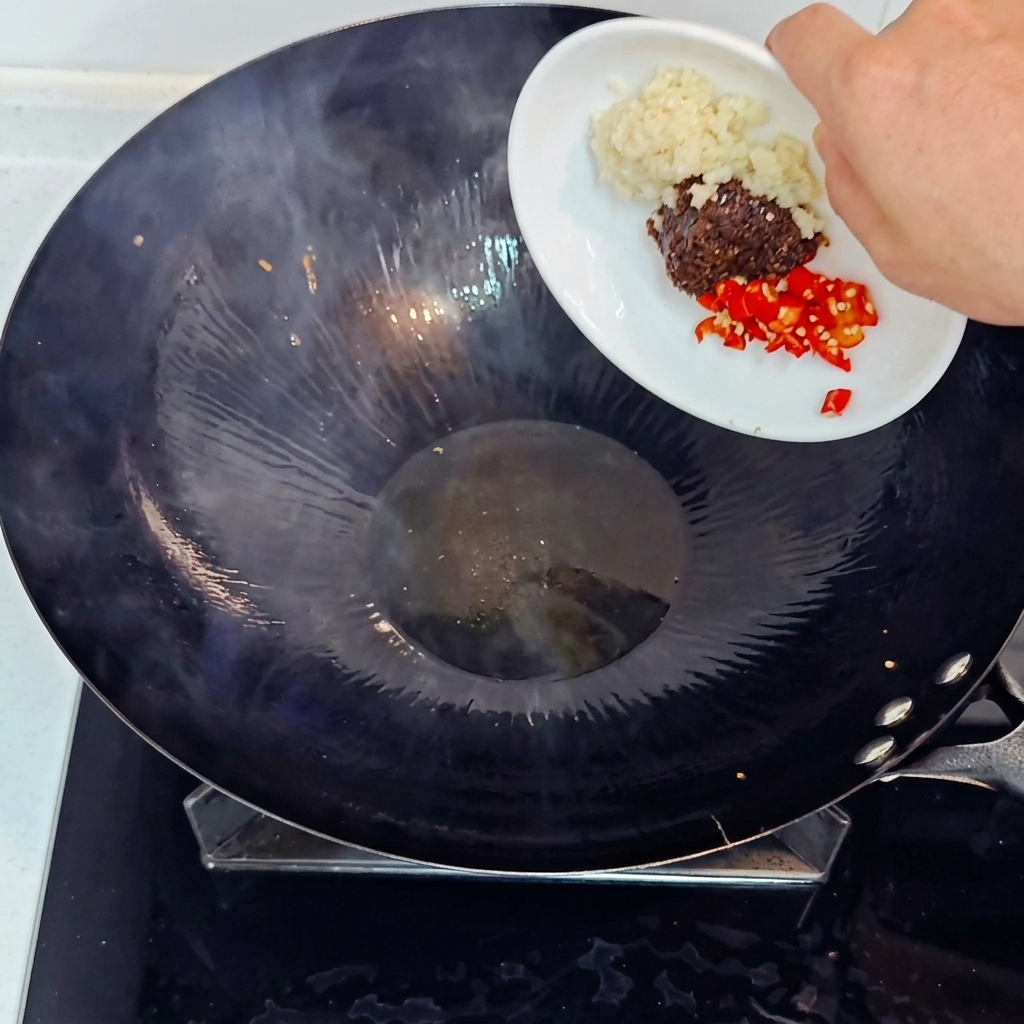 Gehackter Knoblauch, gehackte rote Chili und Sojabohnenpaste werden in einem heißen Wok hinzugefügt.