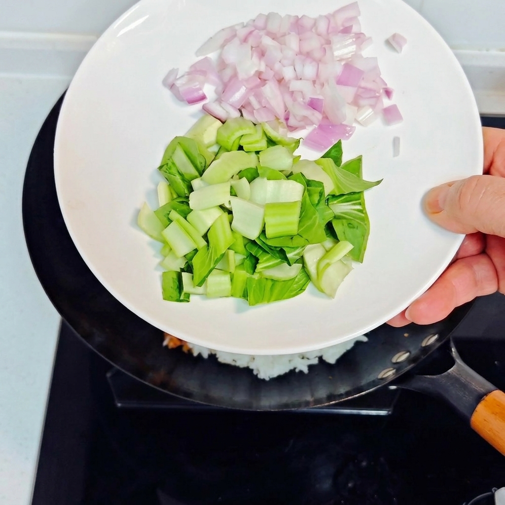 Gewürfelte Zwiebeln und gehackter Bok Choy werden zum Reis in den Wok gegeben.