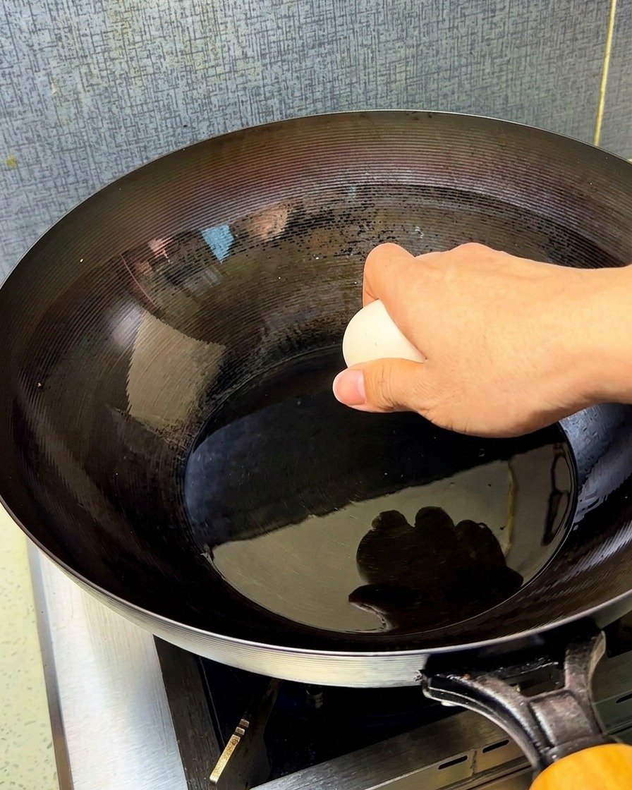 Zwei rohe Eier werden in einen gut gewürzten, heißen Wok mit schimmerndem Speiseöl geschlagen.