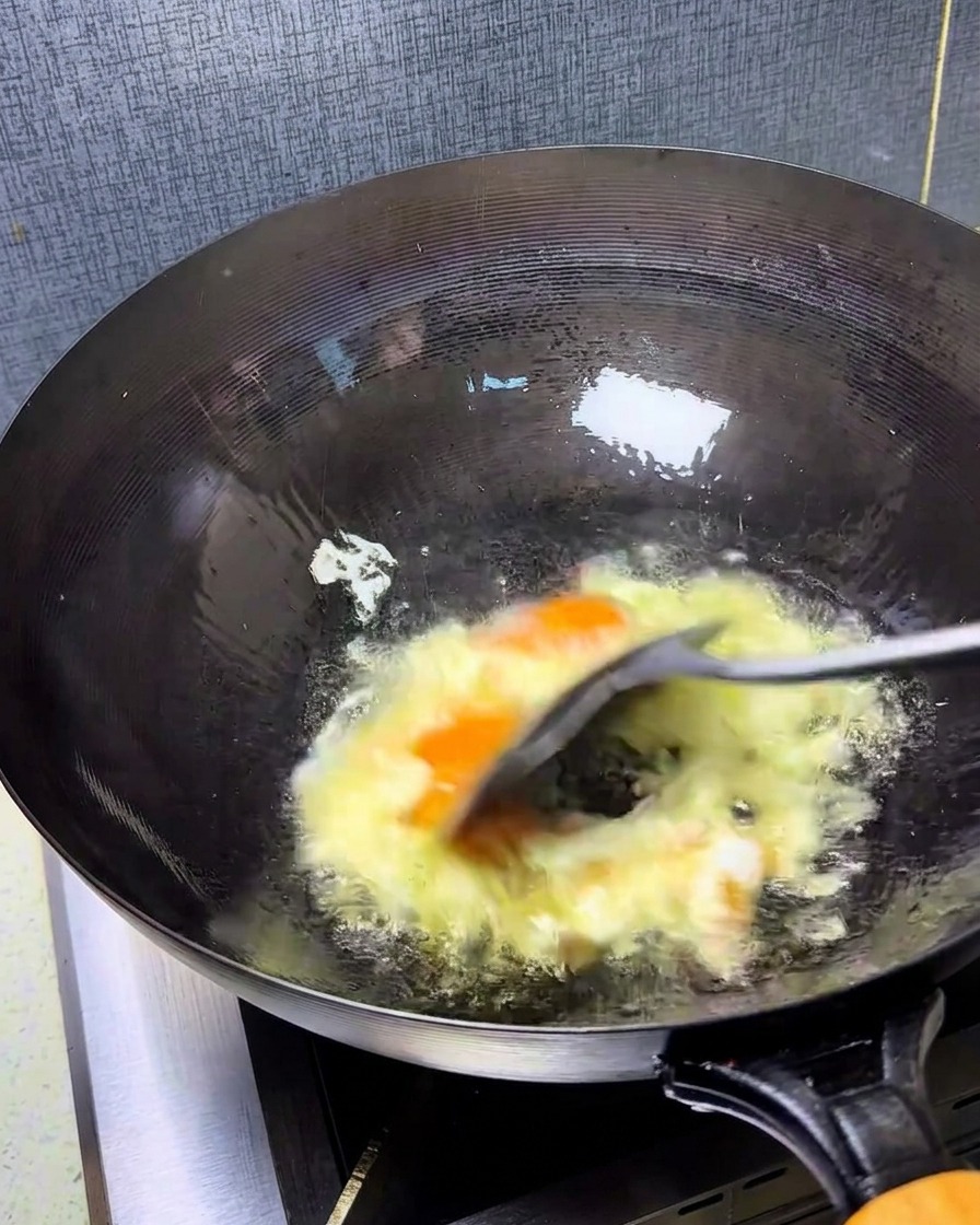Eier werden in einem heißen Wok mit einem Spatel schnell verrührt, sodass lockere, goldene Stücke entstehen.