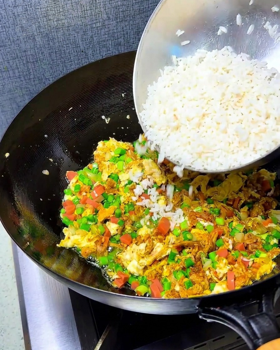 Zerkrümelter weißer Reis wird in den Wok mit den gebratenen Eiern und der Gemüsemischung gegeben.