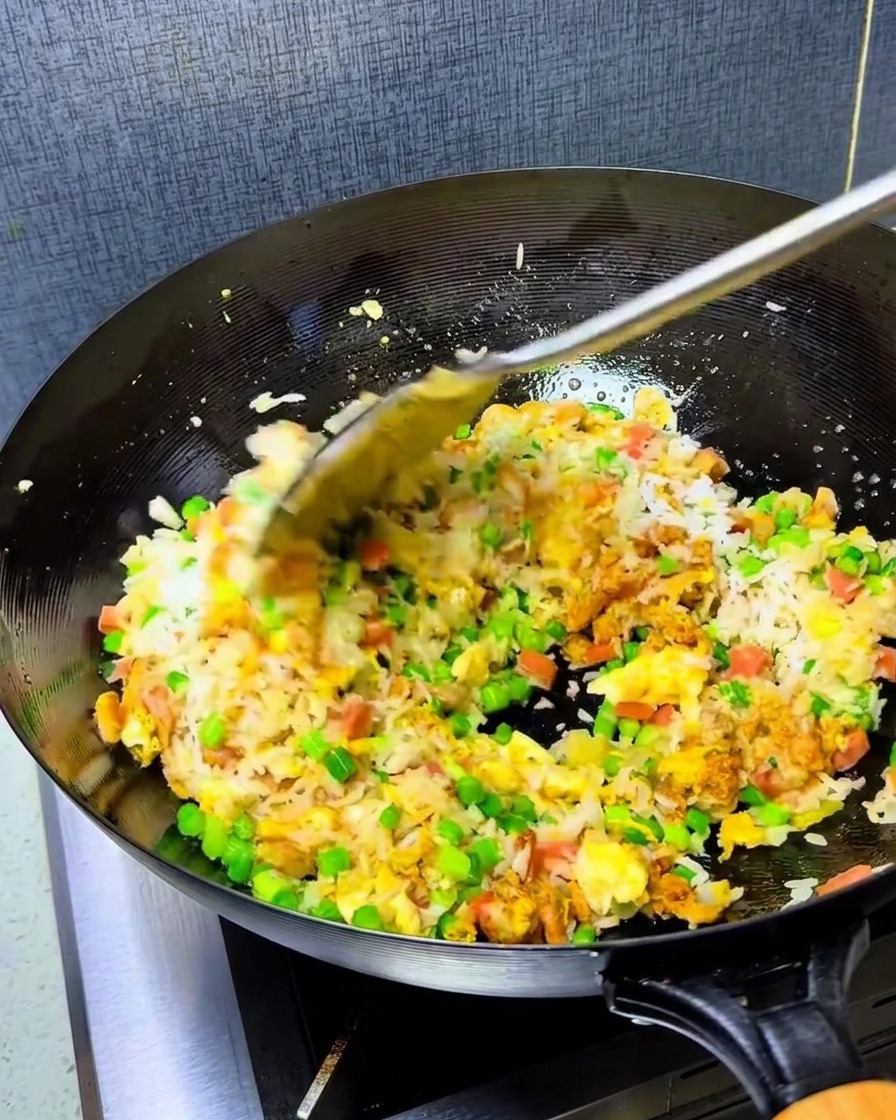 Ein Löffel leuchtend rotes Chiliöl wird zur Reismischung im heißen Wok gegeben.