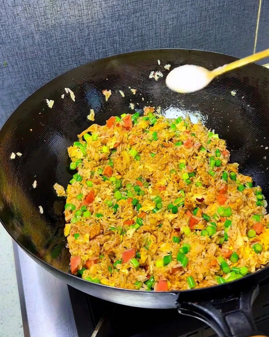 Nahaufnahme von Salz und Hühnerbrühe, die in einen Wok voller bunter Kimchi-Reis-Mischung gestreut werden.