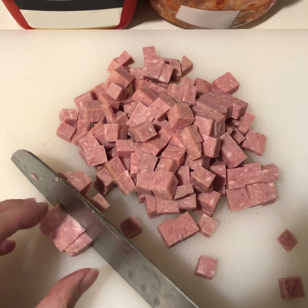 Nahaufnahme von Spam, der auf einer weißen Unterlage in gleichmäßige Würfel geschnitten wird.