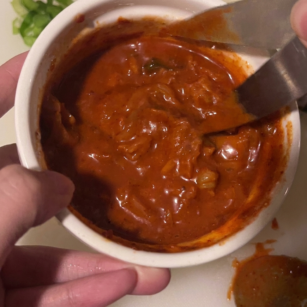 Eine Küchenschere schneidet Kimchistücke direkt in der Schüssel mit der Sauce.