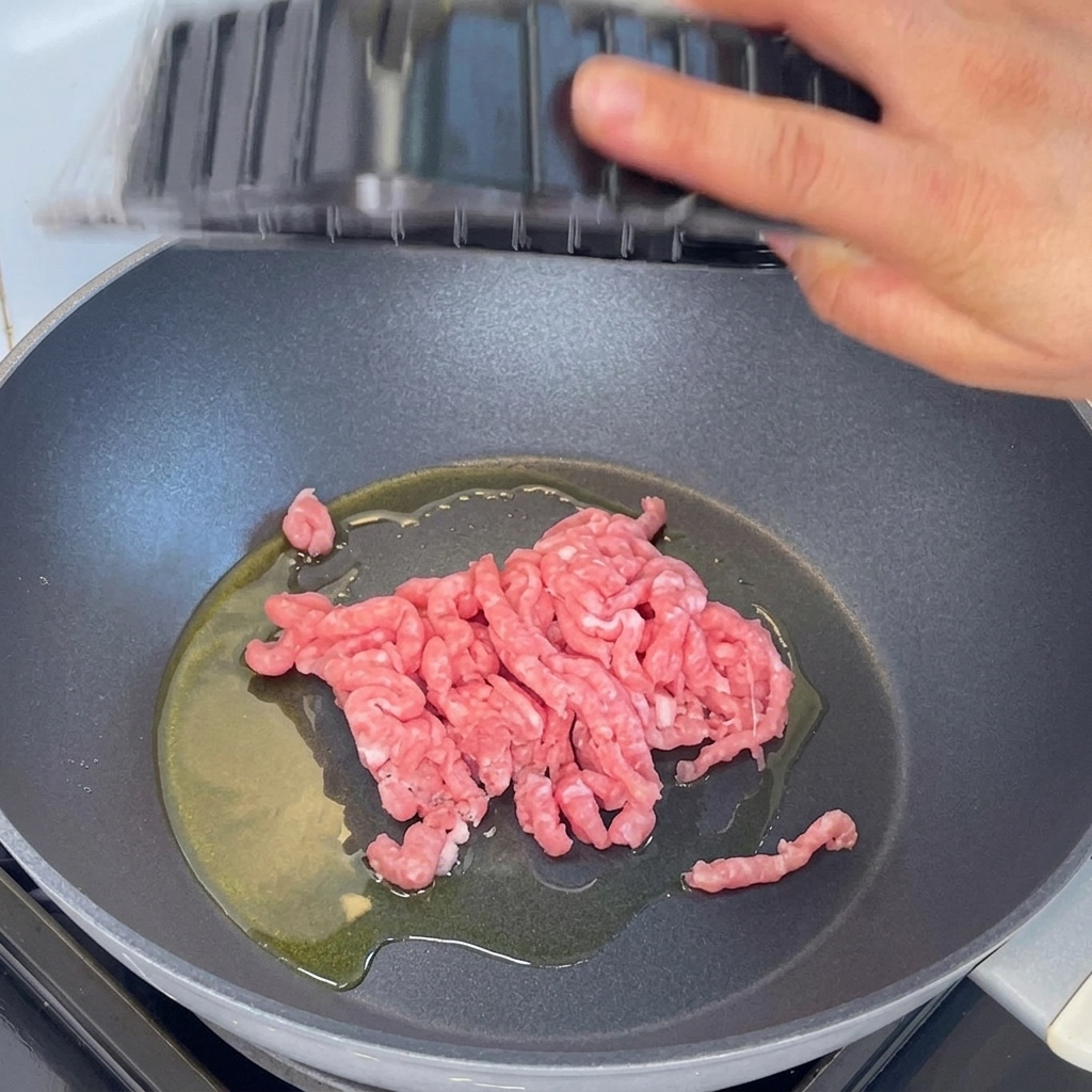 Schweinehackfleisch wird in einer Pfanne mit heißem Öl unter Verwendung eines Holzspatels angebraten.