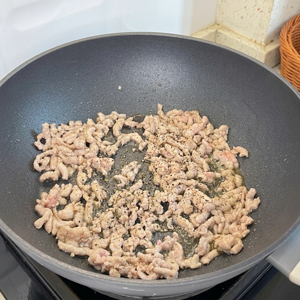 Frisch gemahlener schwarzer Pfeffer wird über das bräunende Hackfleisch in der Pfanne gegeben.