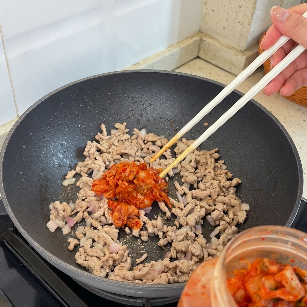 Kimchi-Stücke werden zu der Fleisch-Schalotten-Mischung in die Pfanne gegeben.
