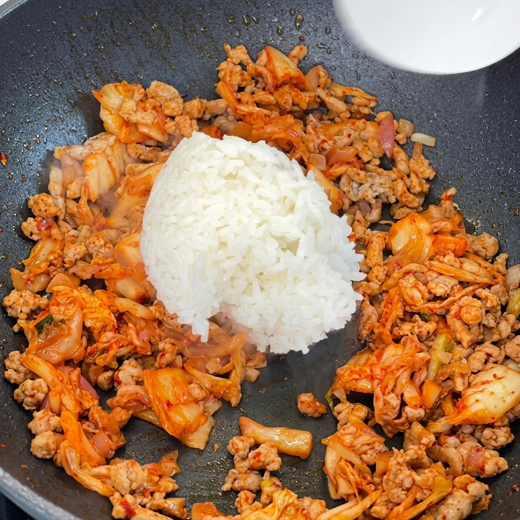 Gekochter weißer Reis wird in die Pfanne zu Fleisch und Kimchi gegeben.