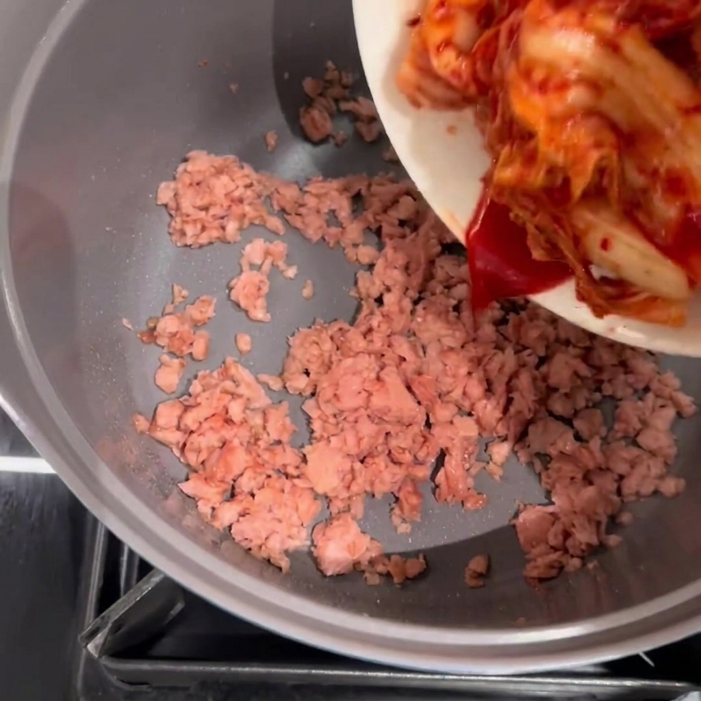Kimchi wird zu einem Topf mit gebräuntem, angebratenem Spam gegeben.