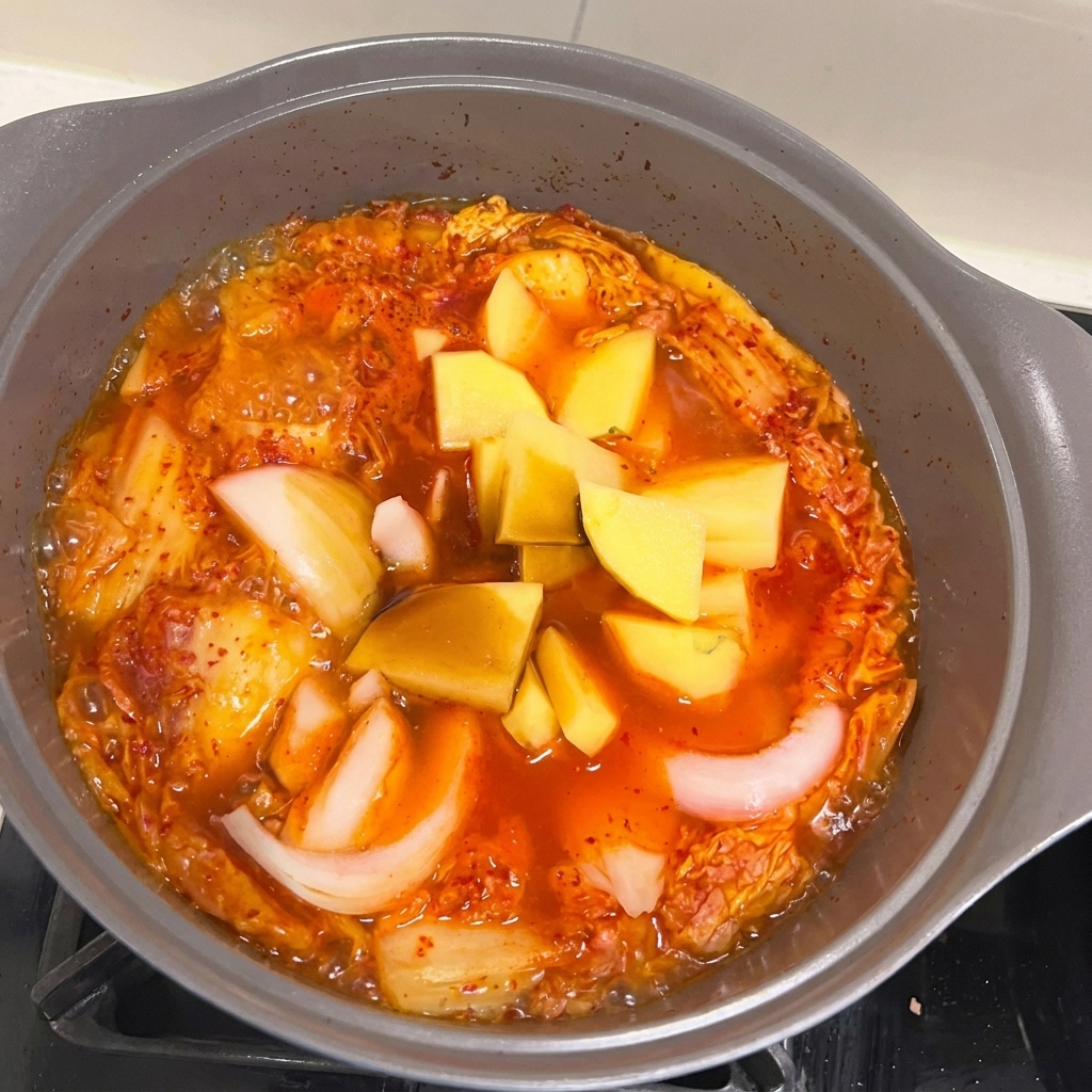 Gehackte Kartoffel- und Zwiebelstücke werden in den blubbernden Spam-Kimchi-Eintopf gegeben.