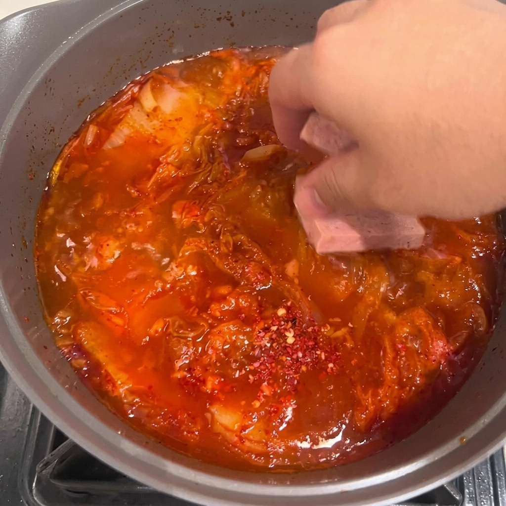 Tofuscheiben werden vorsichtig in den blubbernden roten Kimchi-Eintopf gelegt.