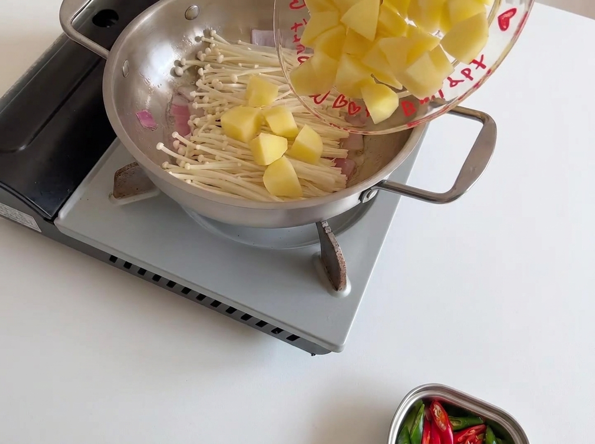 Kartoffelstücke liegen auf dem Pilzbett in der Pfanne.