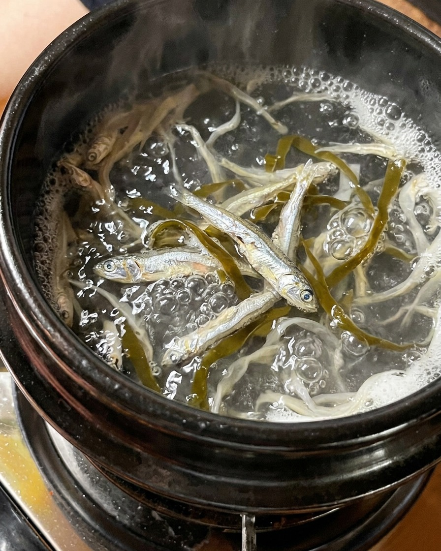 Getrocknete kleine Fische und Seetang kochen in einem Topf mit Wasser.