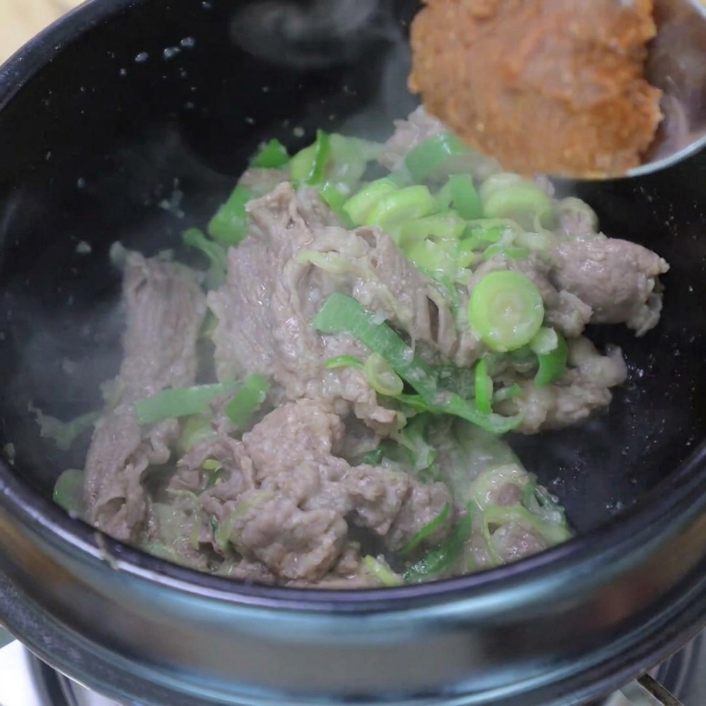 Sojabohnenpaste wird zum angebratenen Fleisch gegeben.
