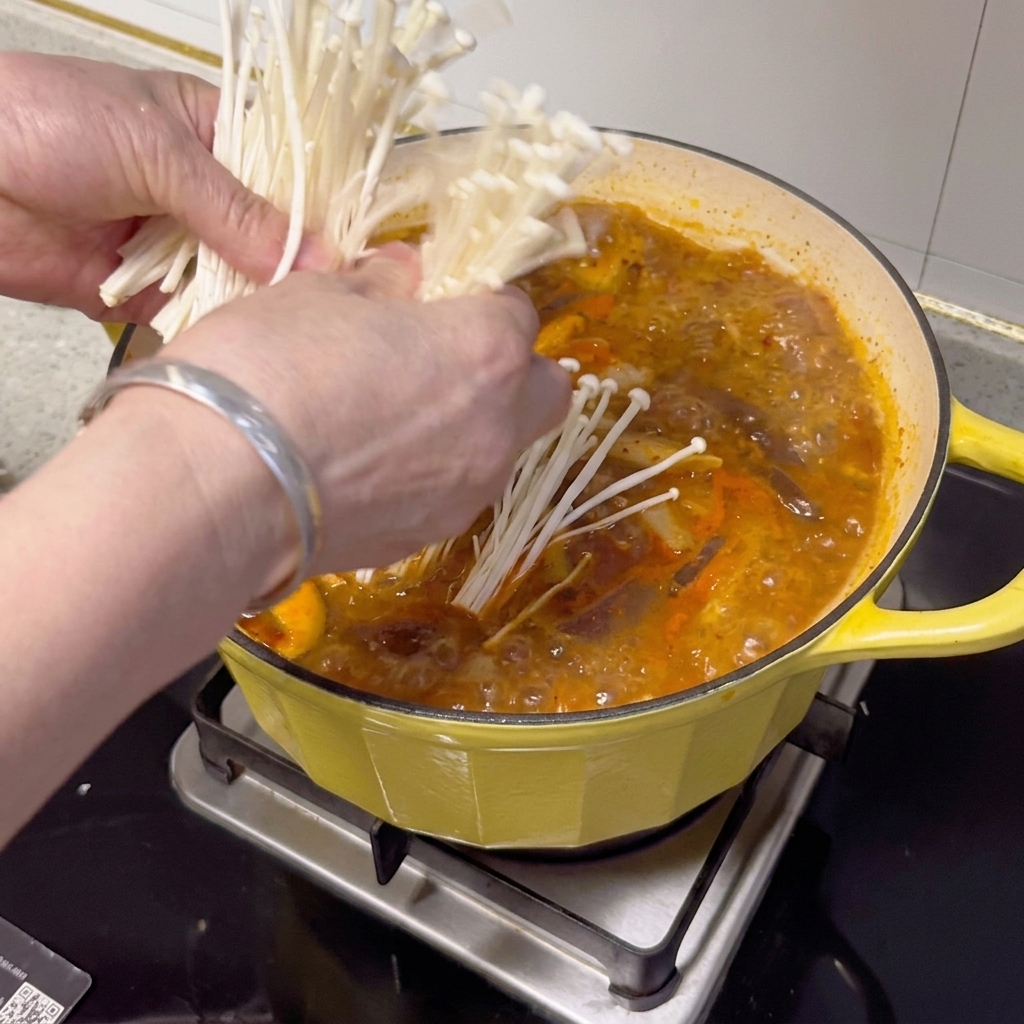 Frische Enoki-Pilze, Frühlingszwiebeln und Chilischeiben werden auf dem fertigen Eintopf drapiert.