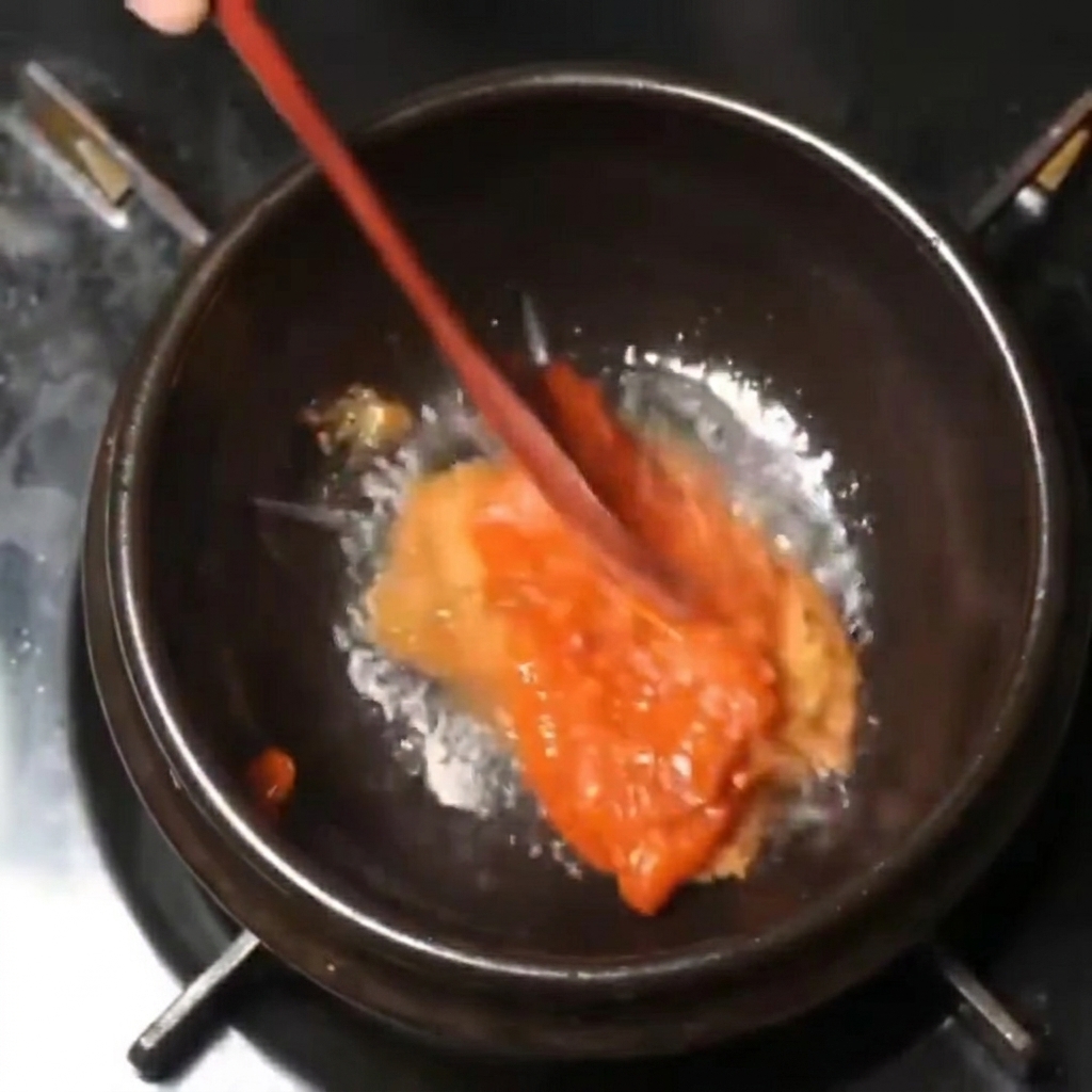 Dicke rote und braune Pastenmischung, die mit einem Holzlöffel in einem schwarzen Topf bei schwacher Hitze umgerührt wird.