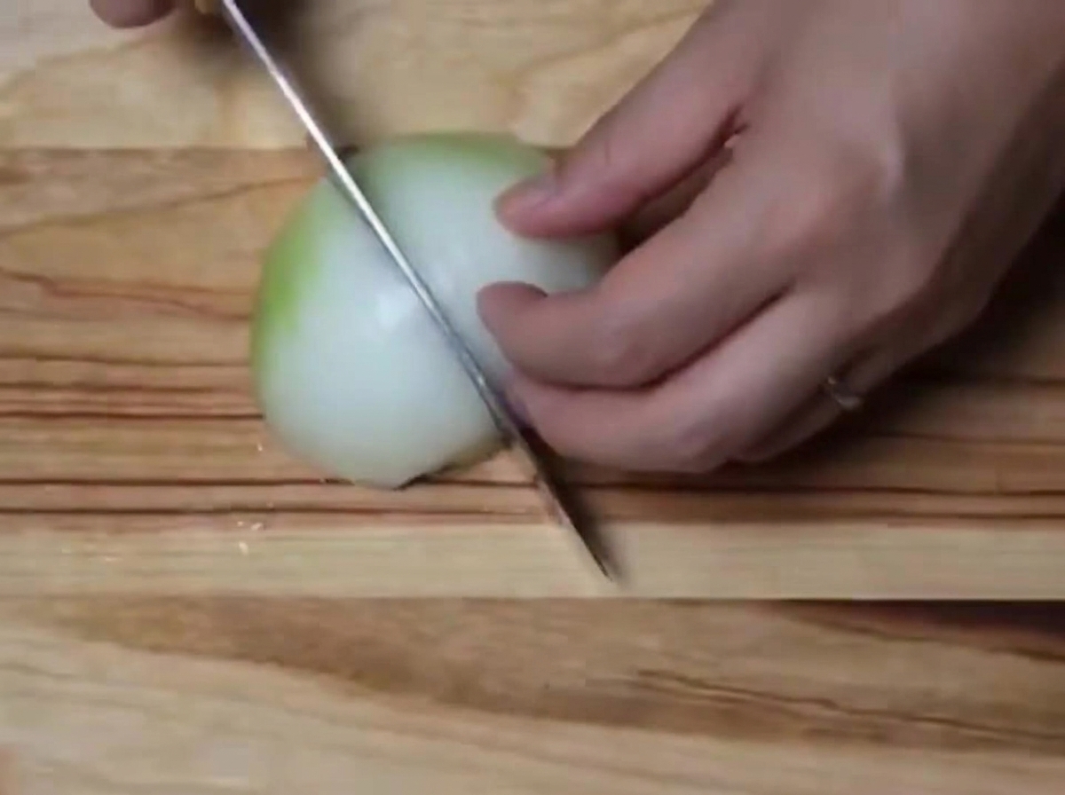 Eine weiße Zwiebel wird auf einem Holzschneidebrett in kleine Stücke gehackt.