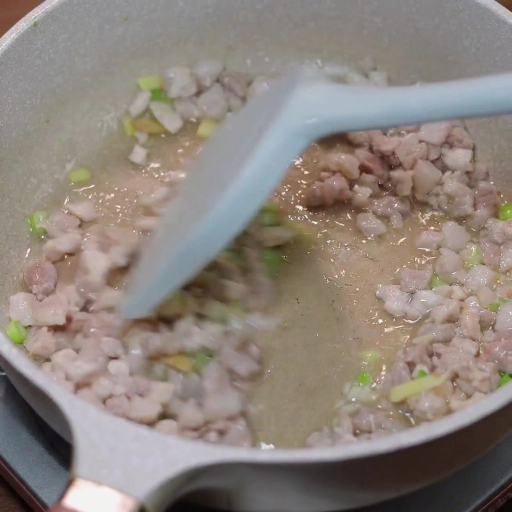 Schweinehackfleisch wird in einer Pfanne mit Frühlingszwiebeln und Ingwer angebraten.