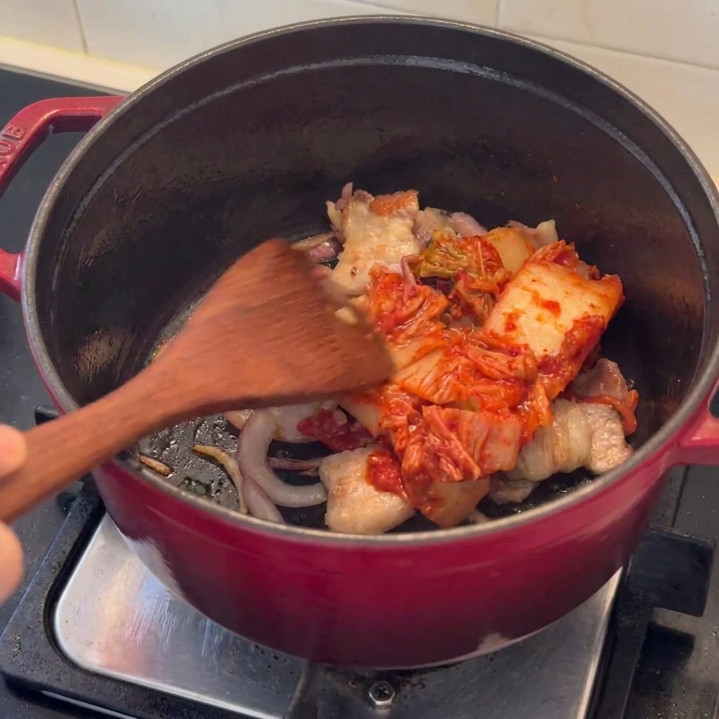 Kimchistücke werden zusammen mit angebratenem Schweinebauch in einem Topf gebraten.