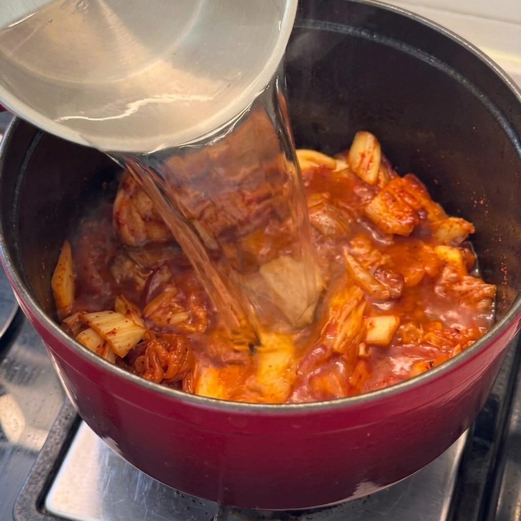 Wasser wird zu Fleisch und Kimchi in den Topf gegossen, um die Eintopfbasis zu bilden.