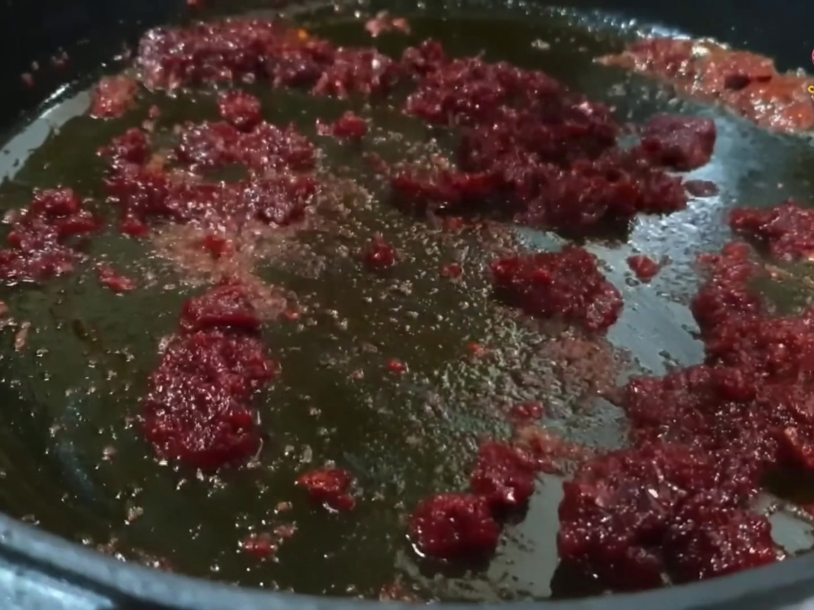 Fleischstücke werden in der Pfanne mit der leuchtend roten Chili-Öl-Mischung vermengt.