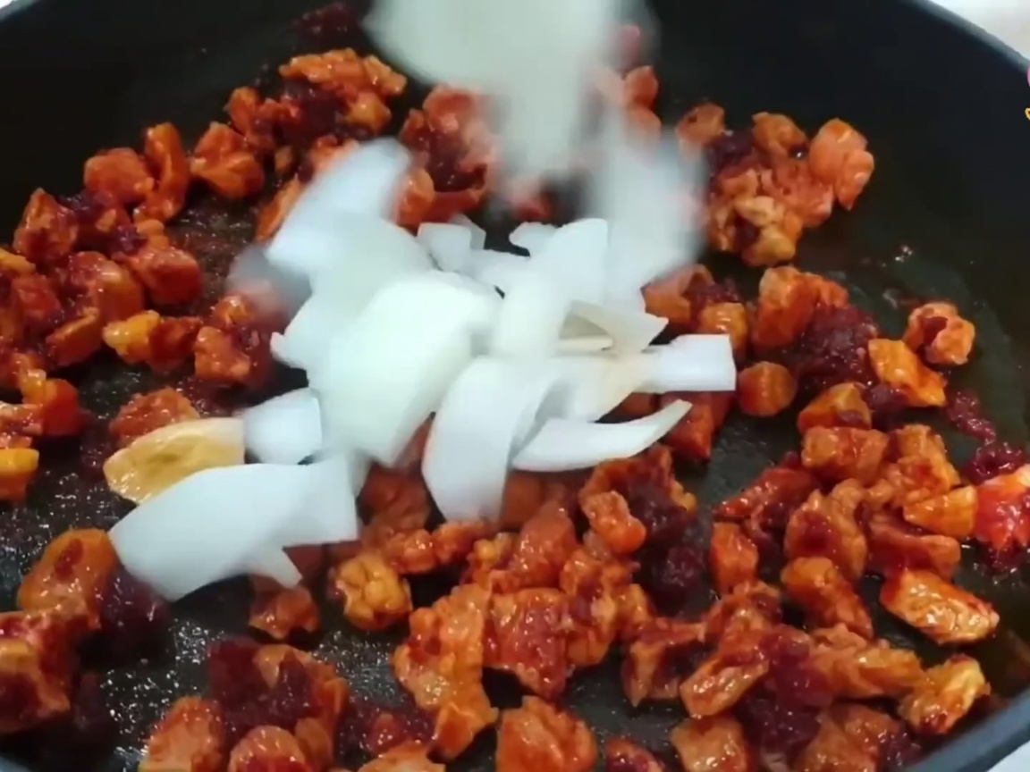Gewürfelte Zwiebel, Frühlingszwiebel und Knoblauch werden zum Fleisch in die Pfanne gegeben.