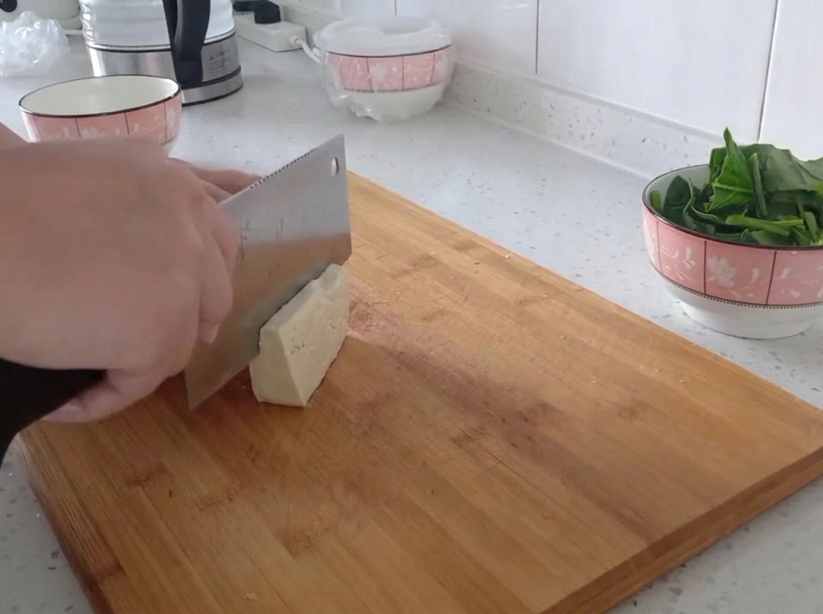 Ein Block fester Tofu, der auf einem Holzschneidebrett in dünne, gleichmäßige Streifen geschnitten wird.