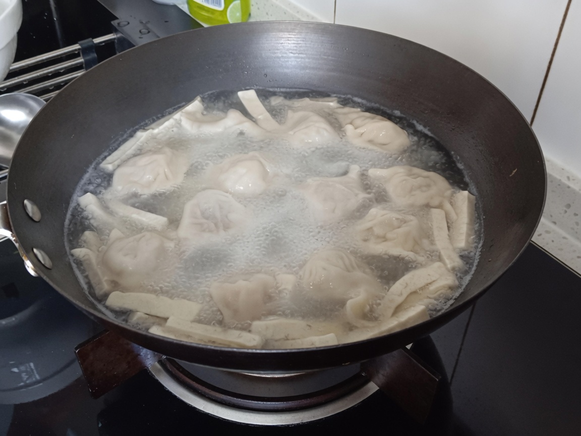 Glasnudeln werden in den kochenden Topf mit Teigtaschen und Tofu getaucht.