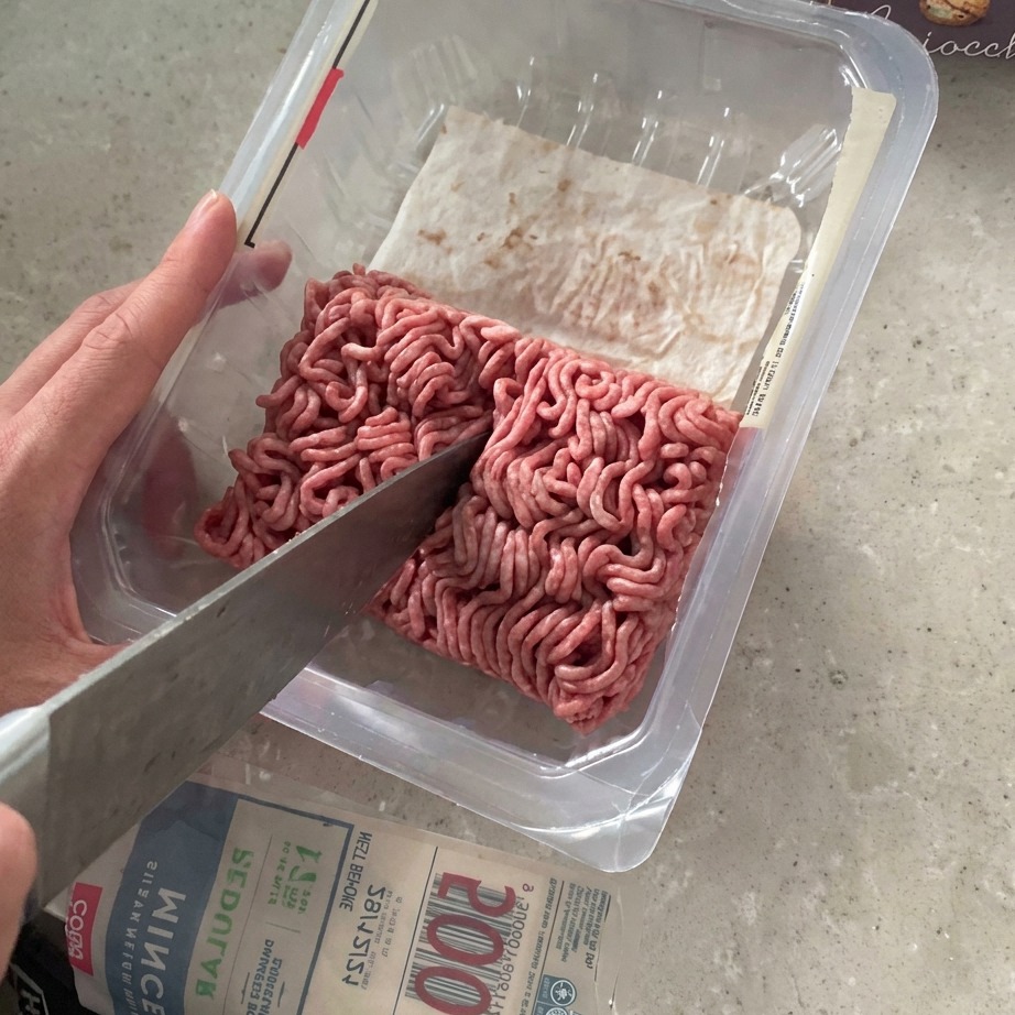 Rinderhackfleisch wird mit einem großen Messer direkt in der Verpackung halbiert.