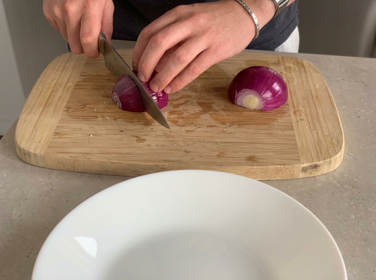 Eine rote Zwiebel wird auf einem Holzschneidebrett in kleine Stücke gehackt.