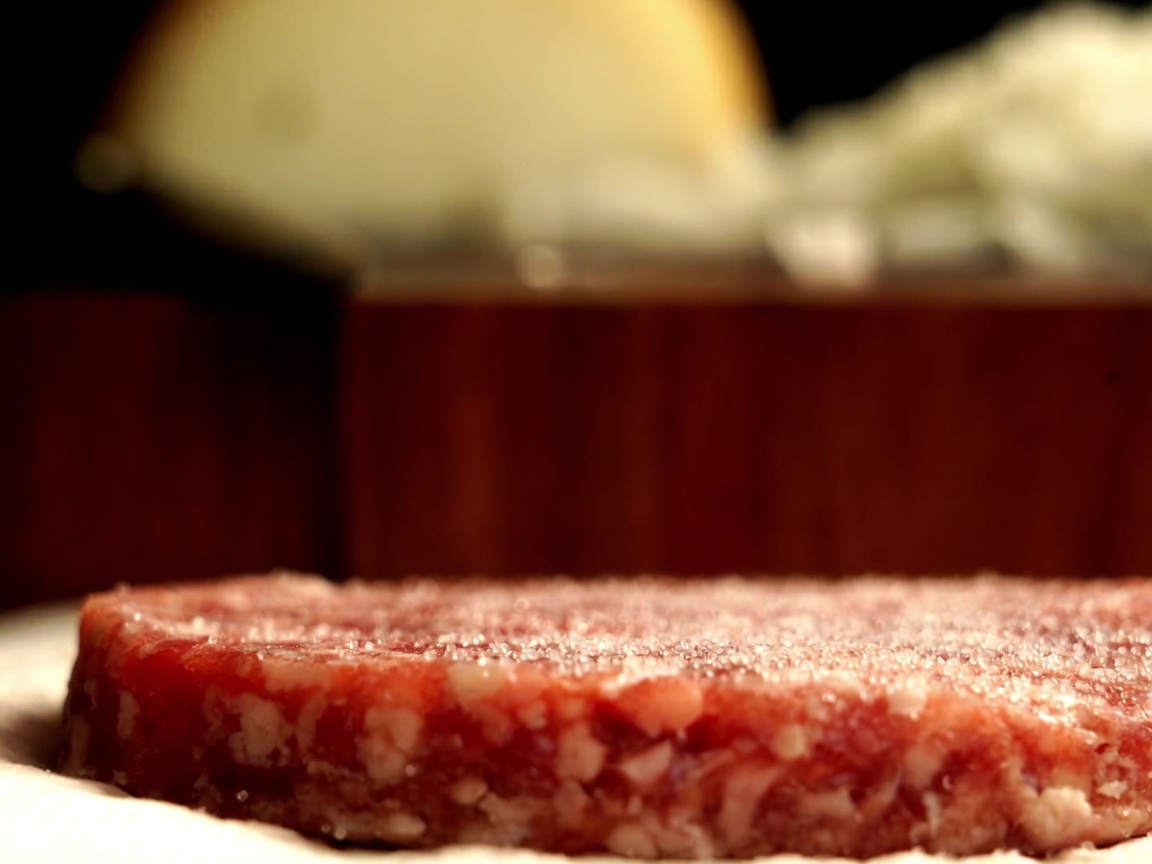 Nahaufnahme eines australischen Wagyu-Pattys, das mit frischem schwarzen Pfeffer aus der Mühle gewürzt wird.