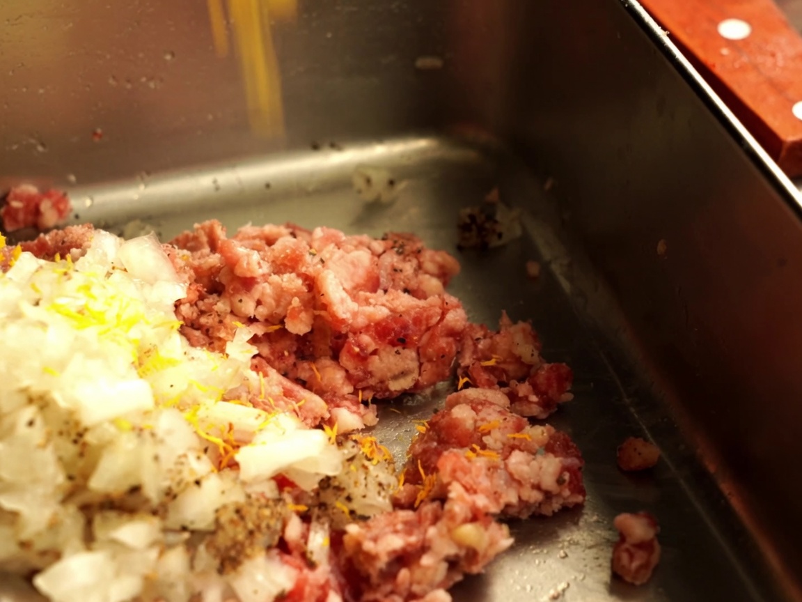 Gehackte Zwiebeln und Paniermehl werden zu rohem Hackfleisch in einer Metallschüssel gegeben.