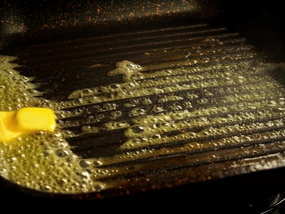 Hälften eines Burgerbrötchens rösten in einer Grillpfanne mit geschmolzener Butter.