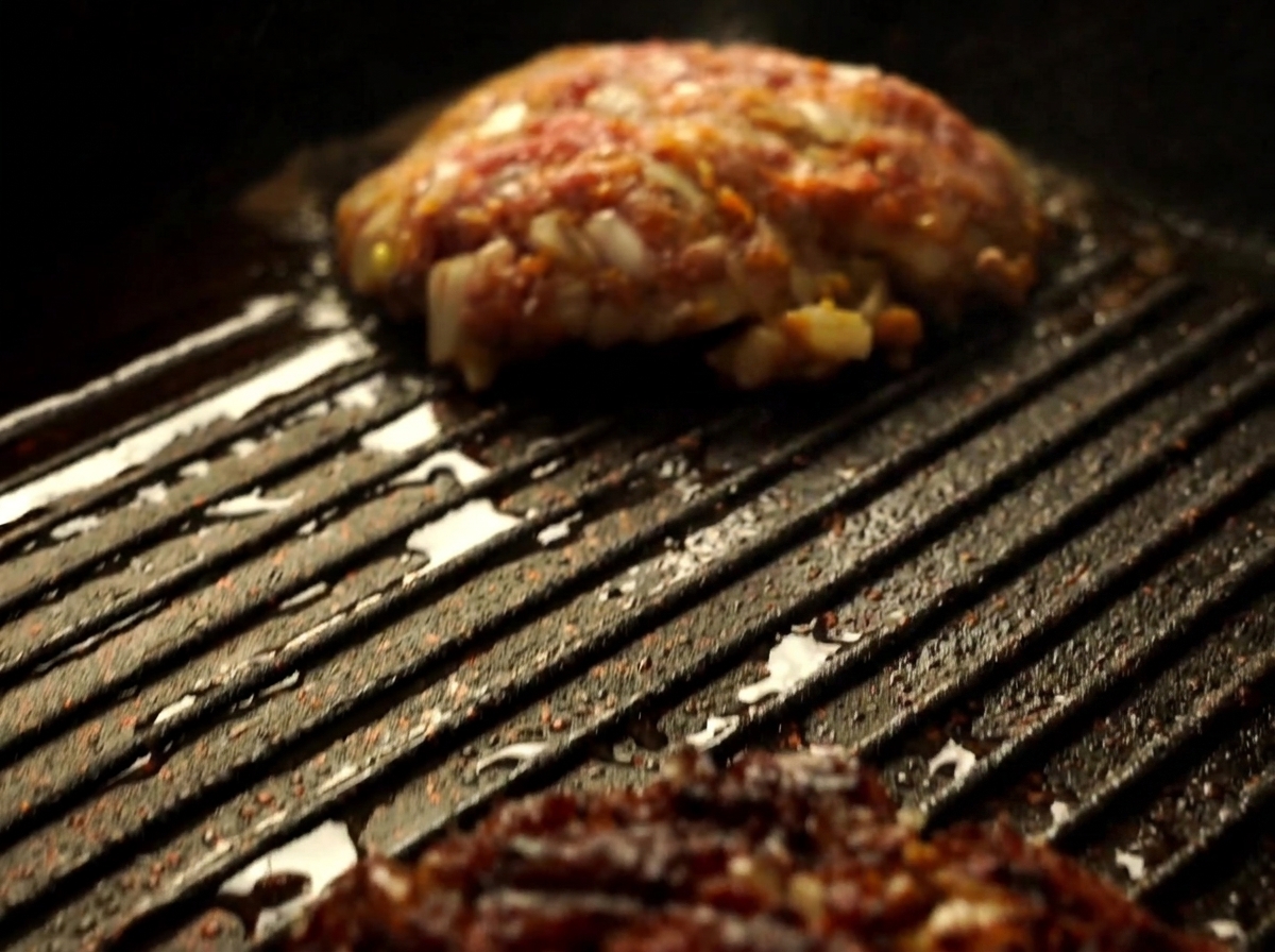 Eine Nahaufnahme eines Wagyu-Rindfleisch-Pattys, das mit einem Spatel in einer heißen Grillpfanne gewendet wird.